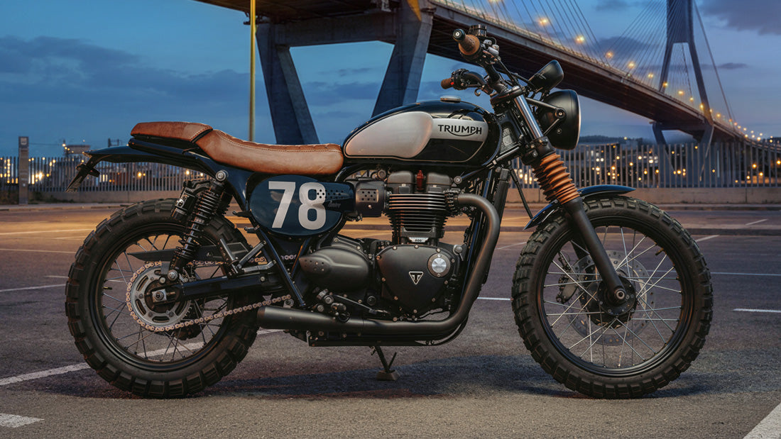 Truimph Motorcycle with '78' on a road at dusk, bridge in the background Redirection for EU site